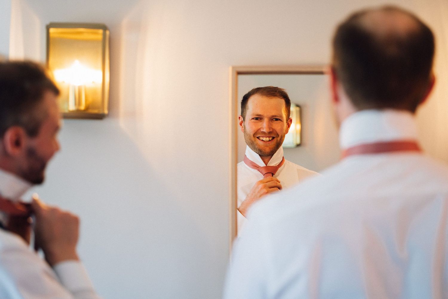 Wedding party getting ready in a bright room with white walls and blue curtains.