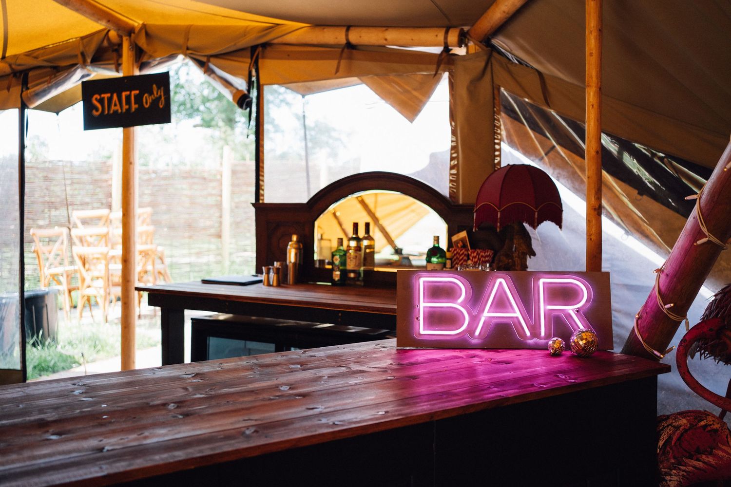 Interior view of a rustic bar area with wooden beams and pink neon lighting.