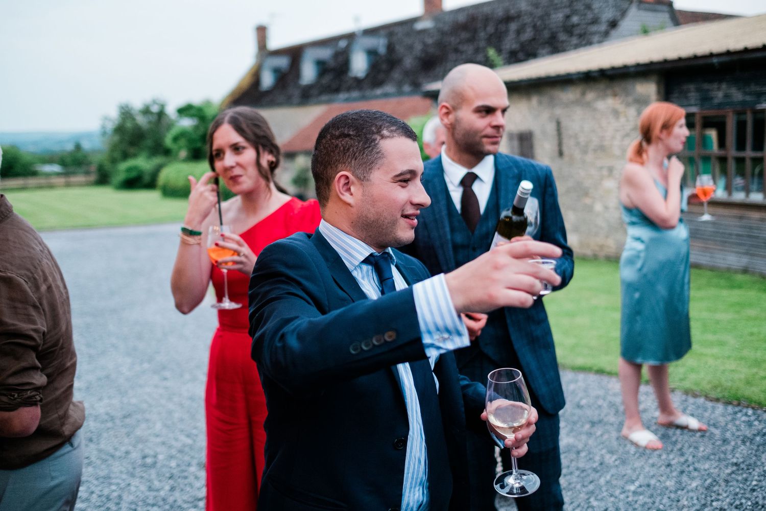 Wedding guests laugh and socialize during an outdoor reception at a rustic stone venue.