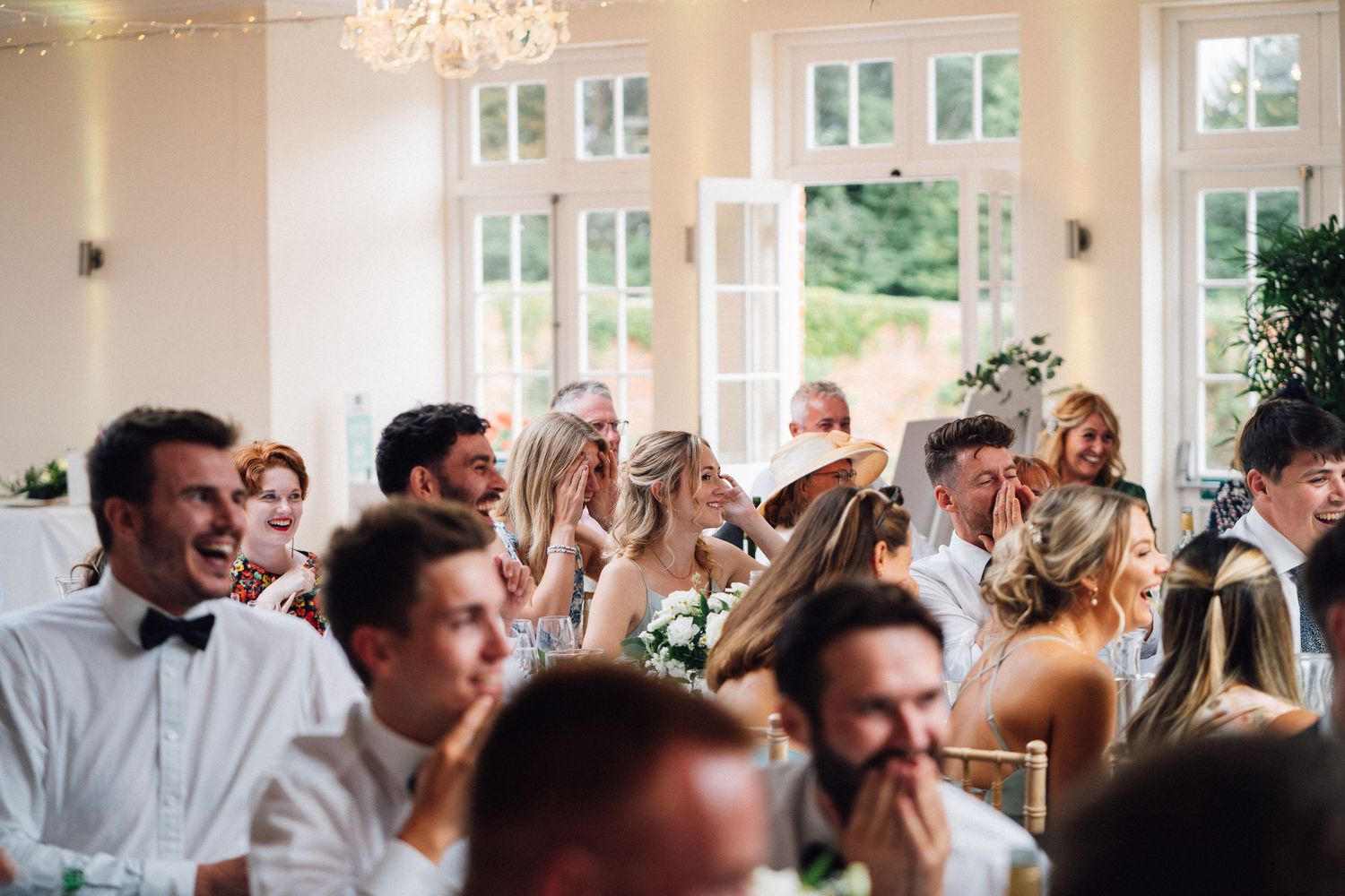 Wedding reception guests laughing and celebrating under an elegant crystal chandelier.