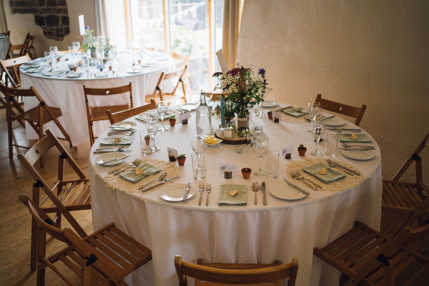 Round dining table with white linens and wooden chairs set for a wedding reception.