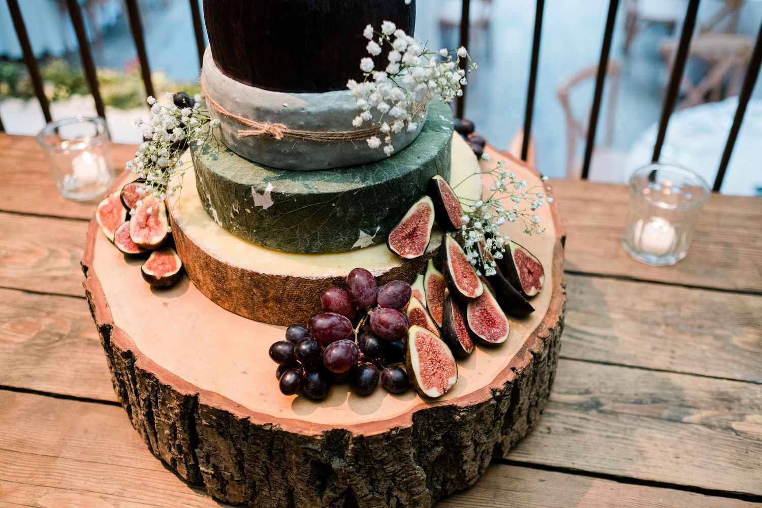 Wedding cake adorned with fresh fruit and flowers on a natural wood slice platter.
