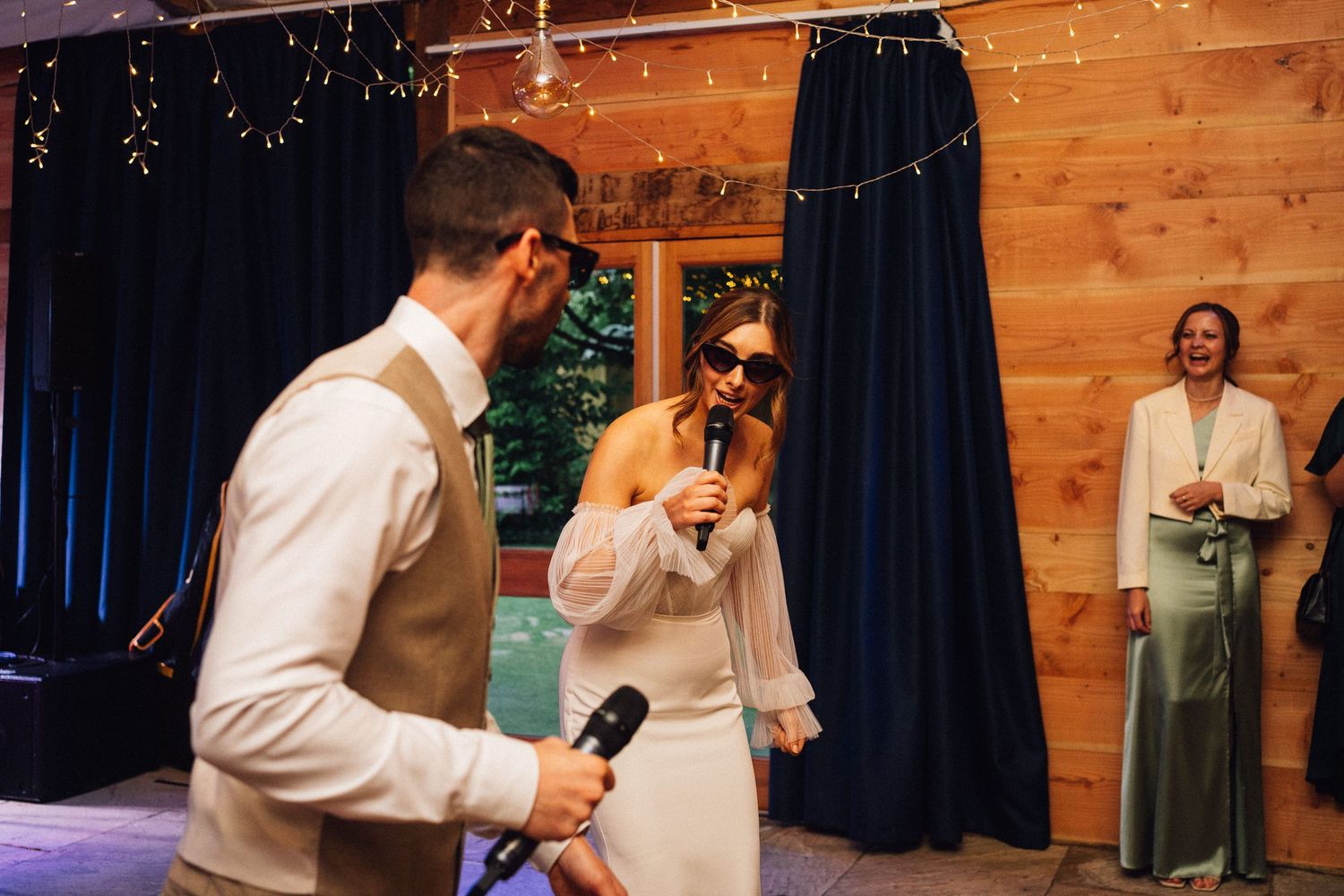 People performing with microphones at rustic indoor venue with string lights.