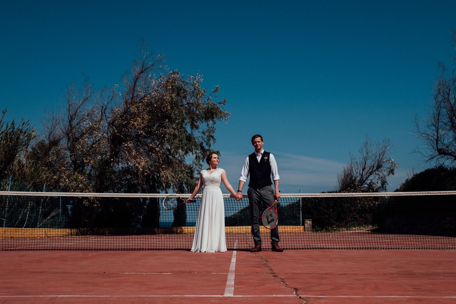 Wedding couple walking on a red-tinted surface with blue sky in background.