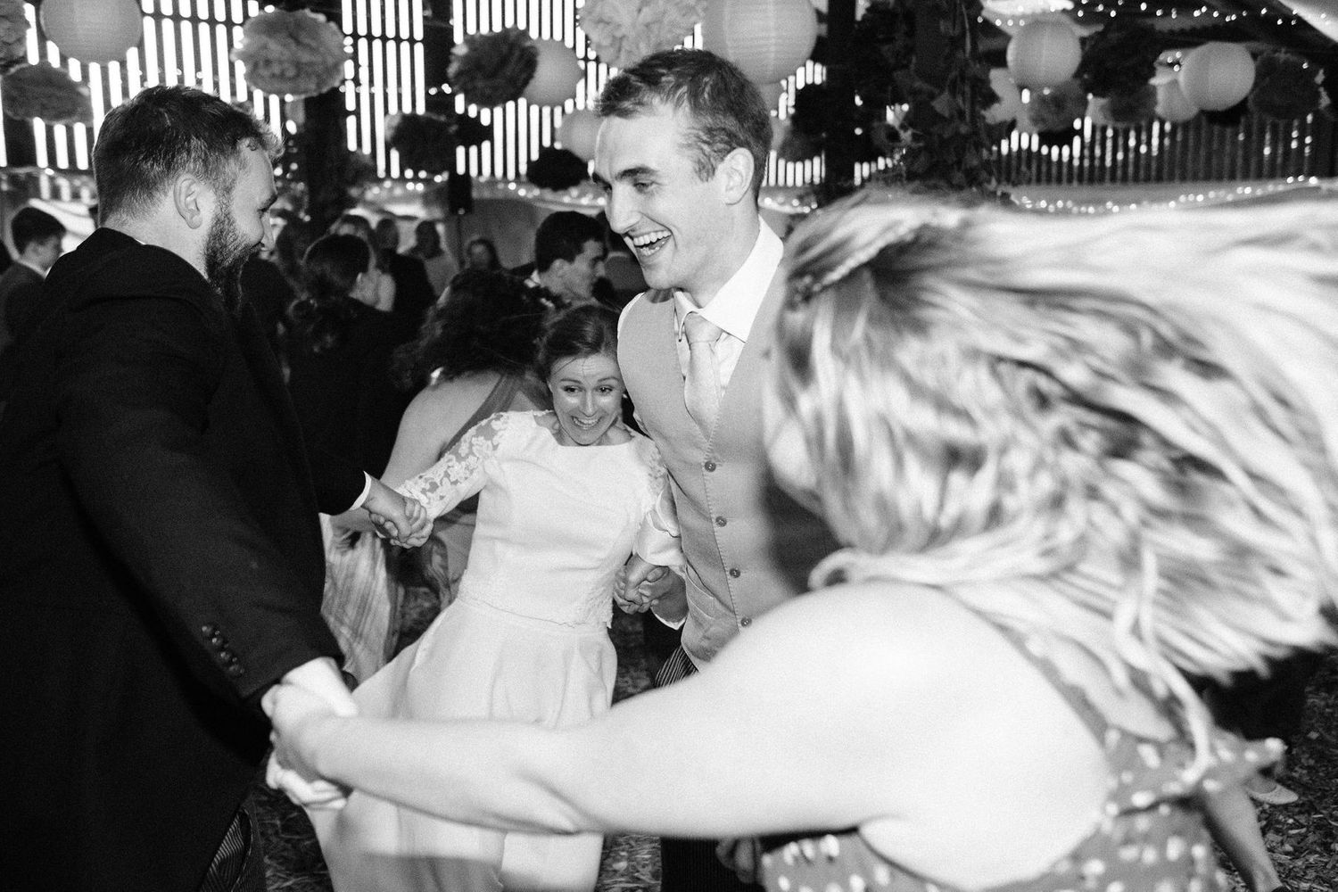 Wedding party guests dancing energetically on a crowded dance floor with dramatic lighting.