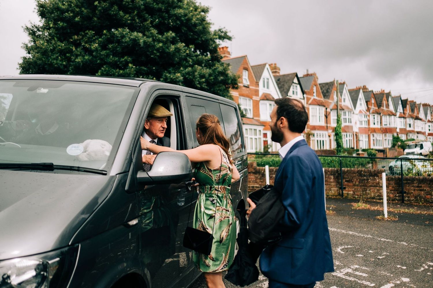Wedding guests gather outside a brick building on an overcast day.