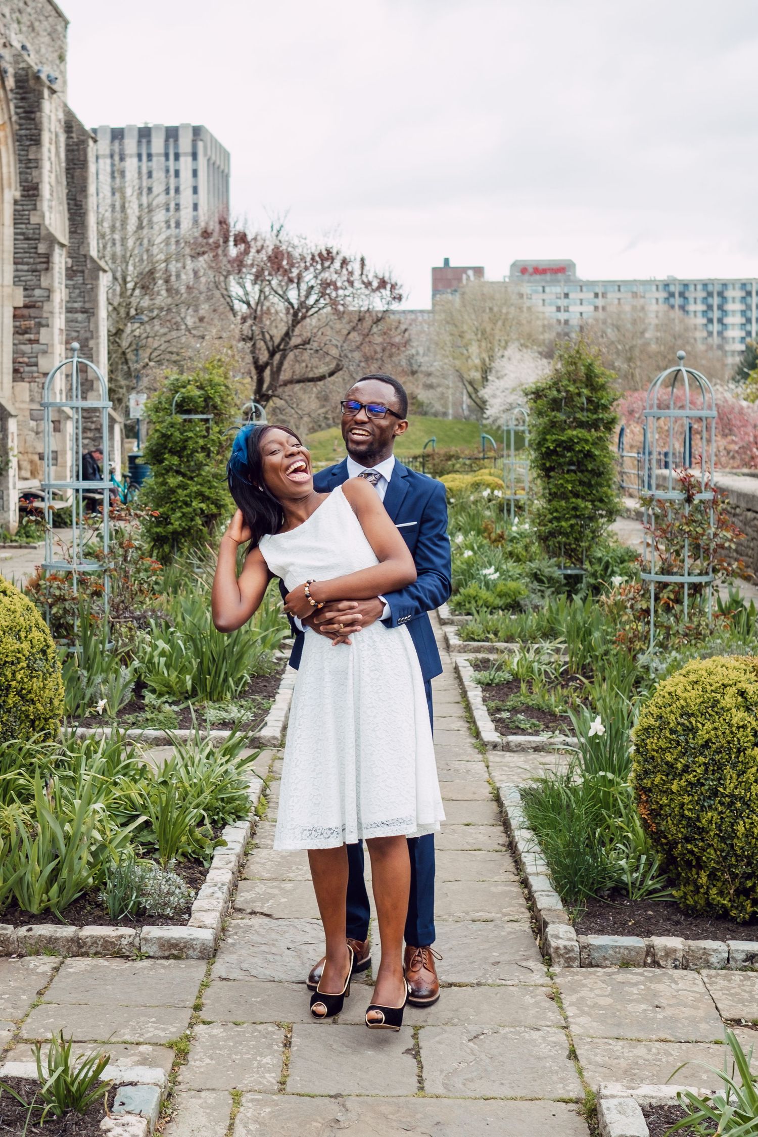 A couple poses playfully in a garden pathway with stone borders and spring flowers.