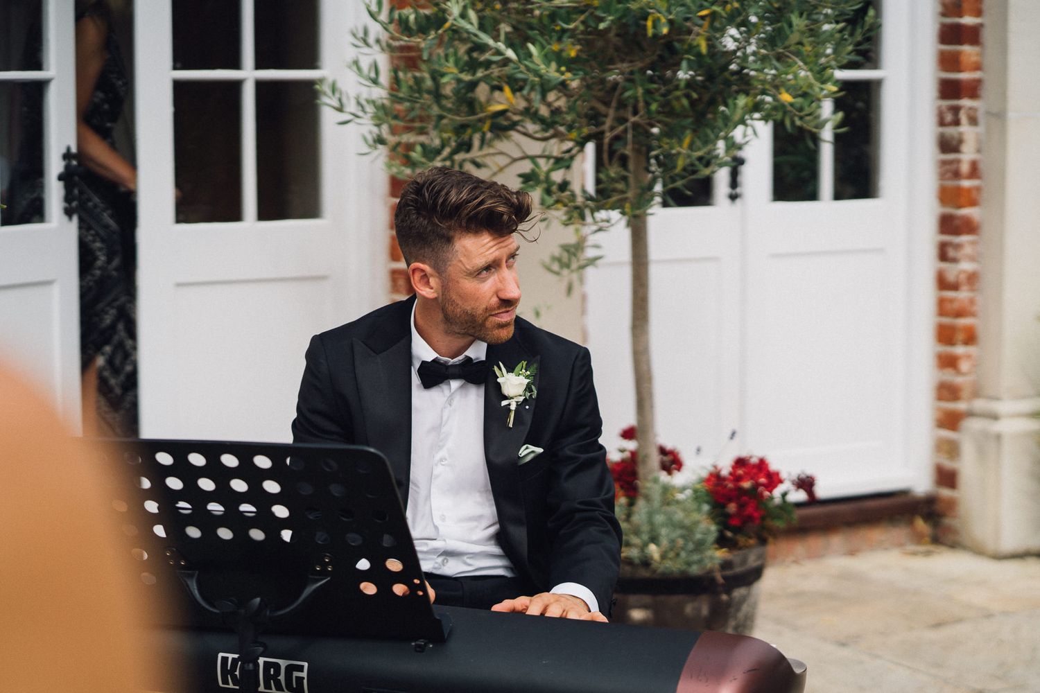 Musicians perform at an outdoor wedding venue with white doors and brick walls.