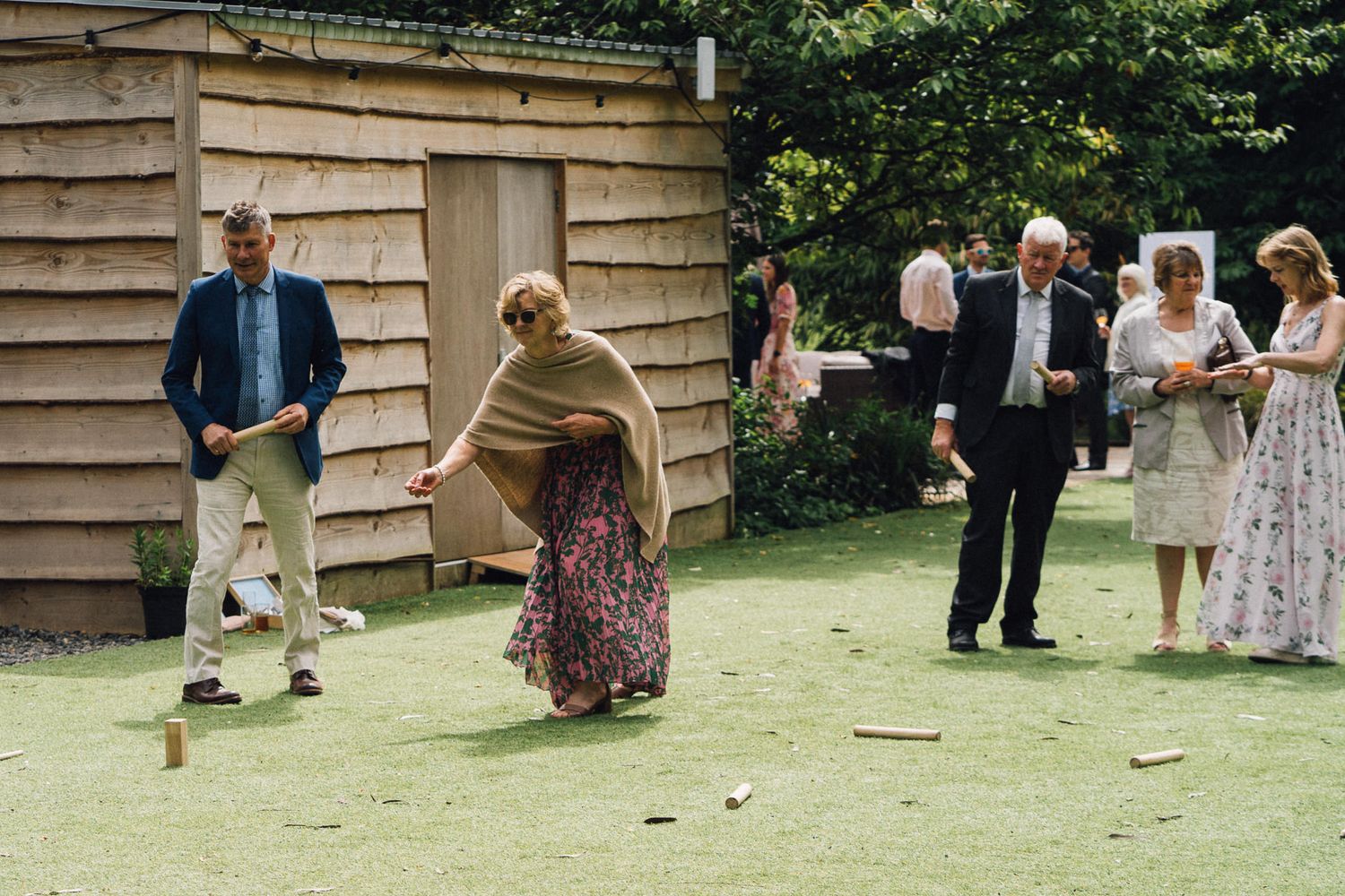 Wedding guests playing lawn games outside a rustic wooden building.