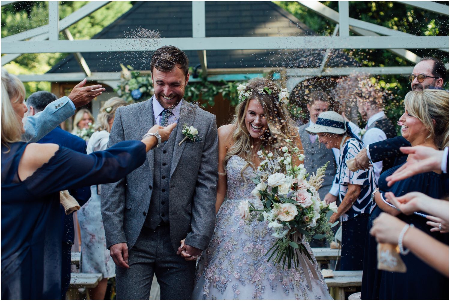 Wedding party and guests celebrate outdoors with confetti and joy.
