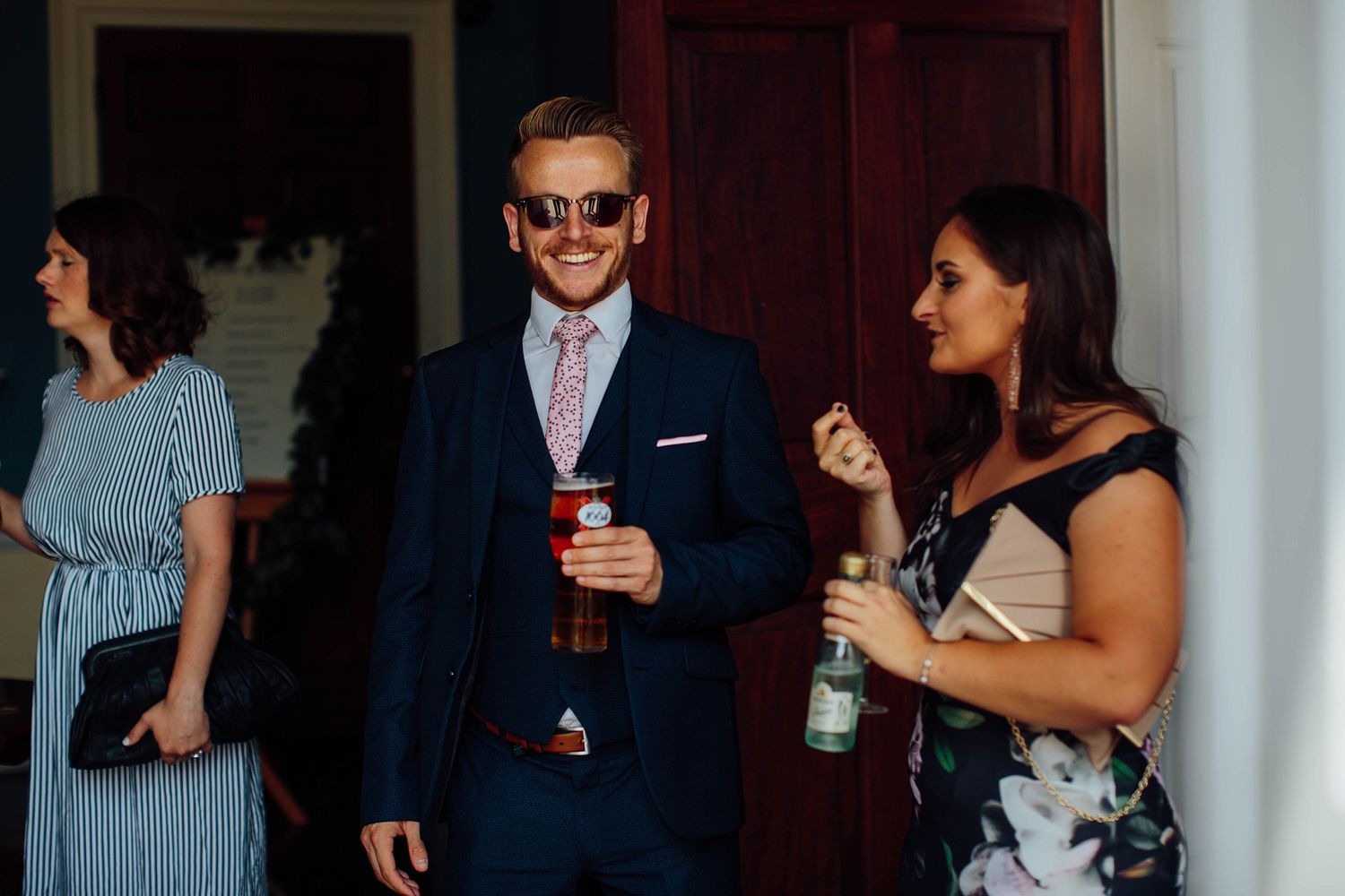 Wedding guests socialize in front of elegant white columns and burgundy doors.