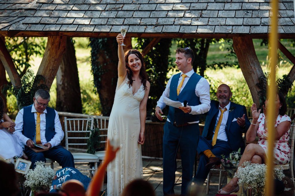 A couple stands under a wooden gazebo during their outdoor wedding ceremony.