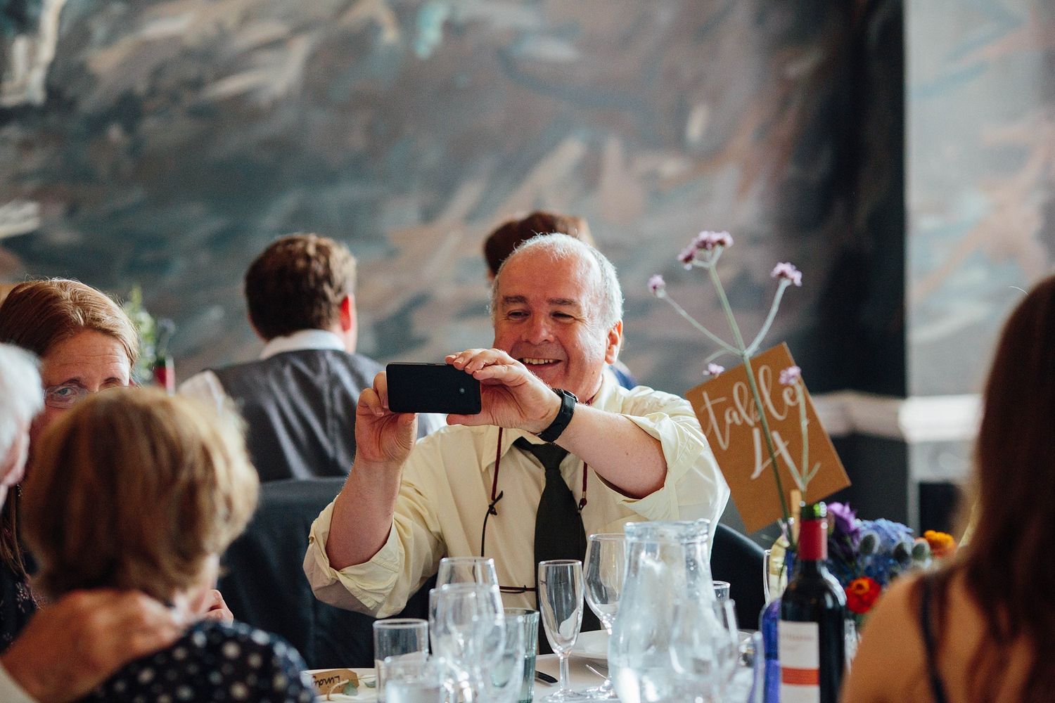 Wedding guest enjoying drinks and conversation at reception with artistic backdrop.