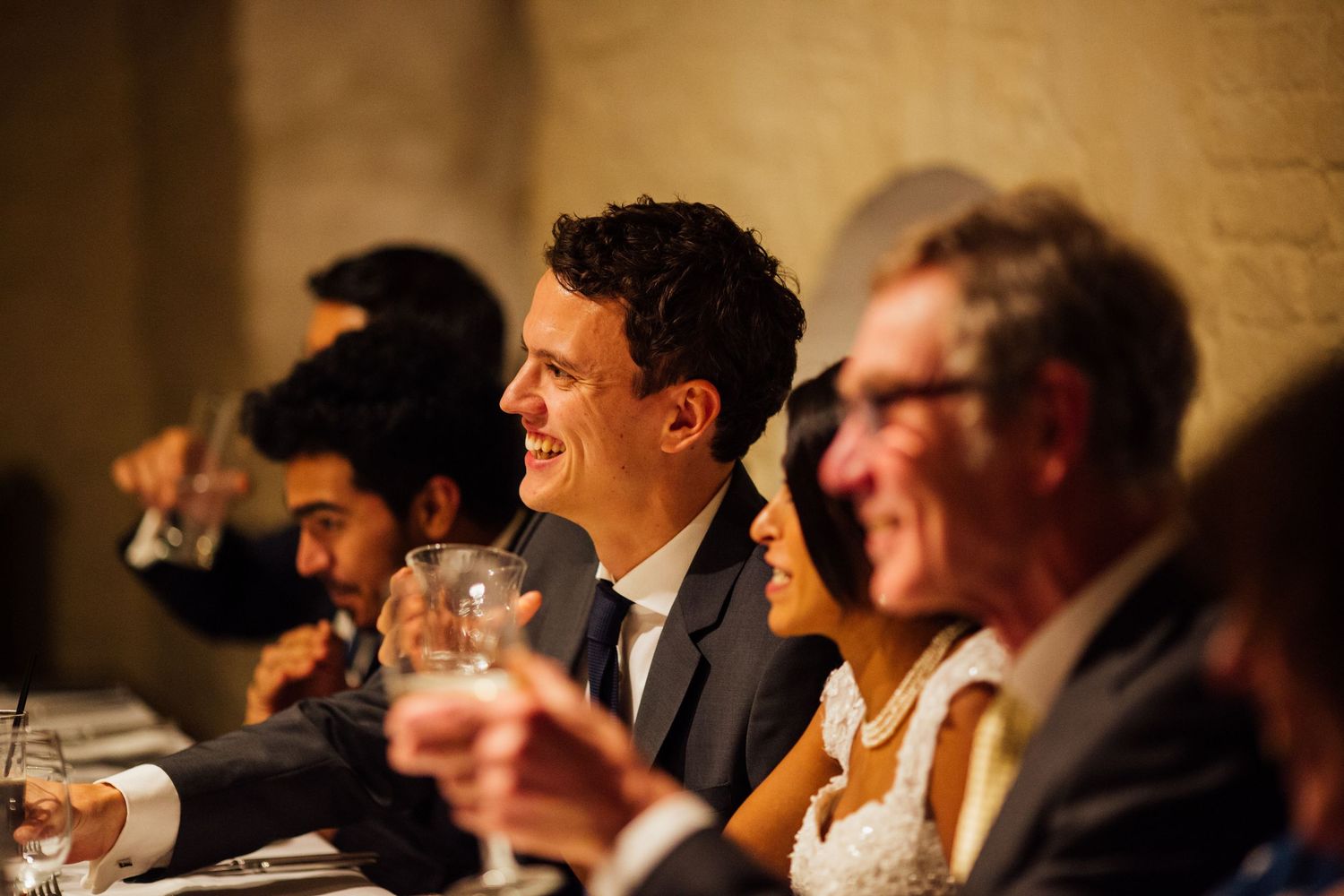 People seated at a formal dinner event share laughter and conversation in a warmly lit banquet hall.