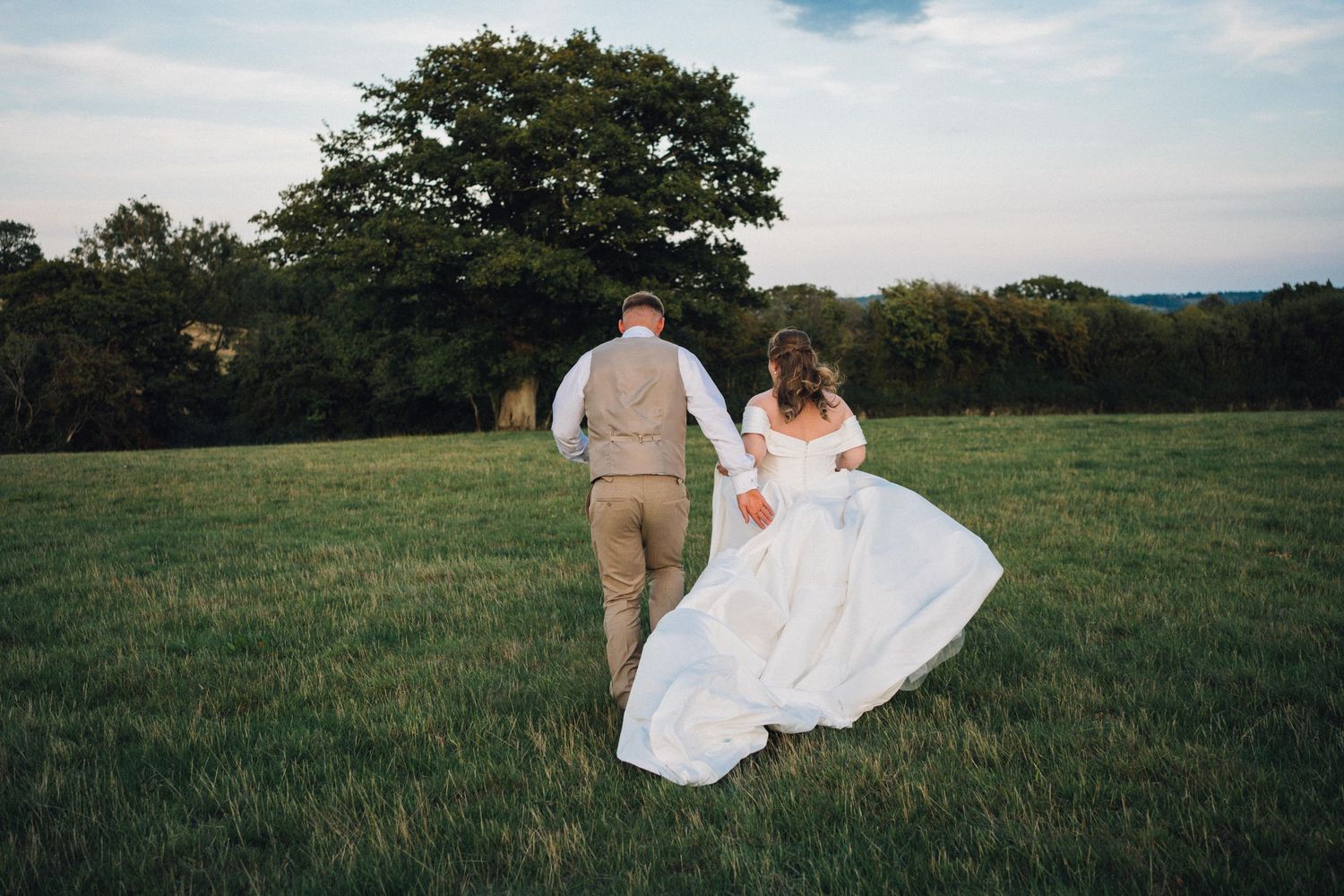 A couple in wedding attire walks together through a lush green meadow on their special day.