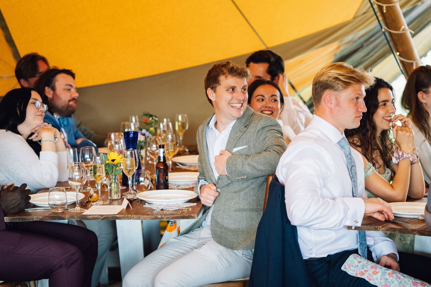 Wedding guests enjoying a celebration inside a large tent with warm lighting.