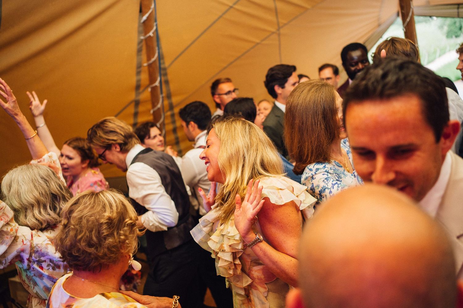 Wedding guests dance and celebrate together under a large tent at a lively reception party.