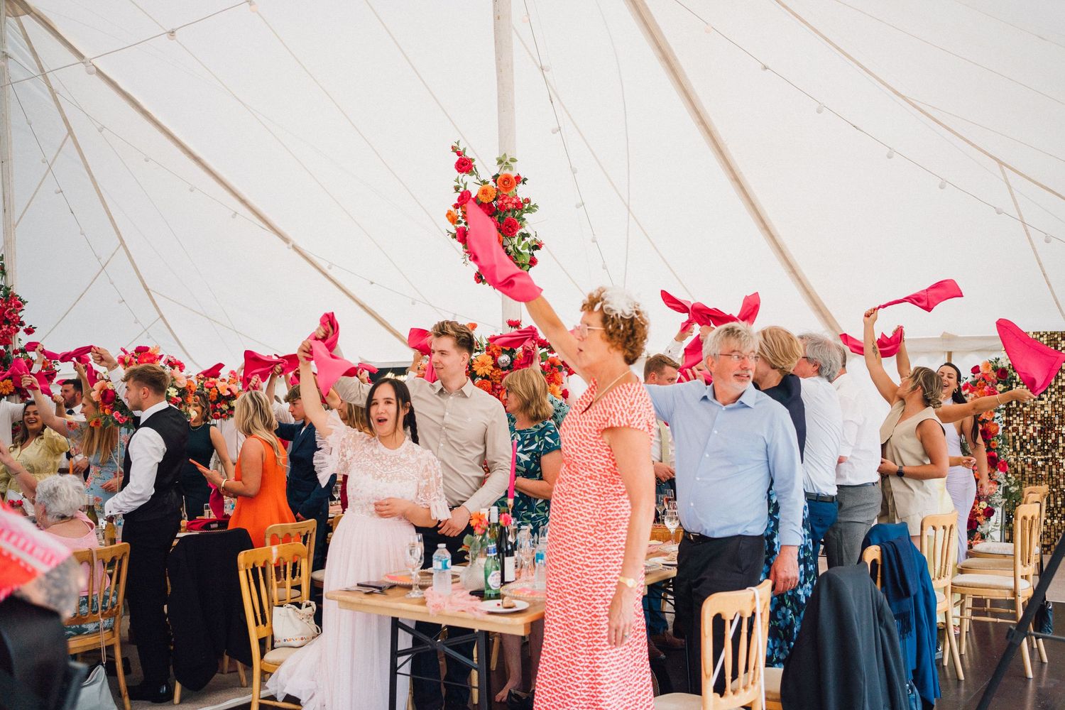 Wedding guests dance and celebrate together under a white tent during an outdoor reception celebration.