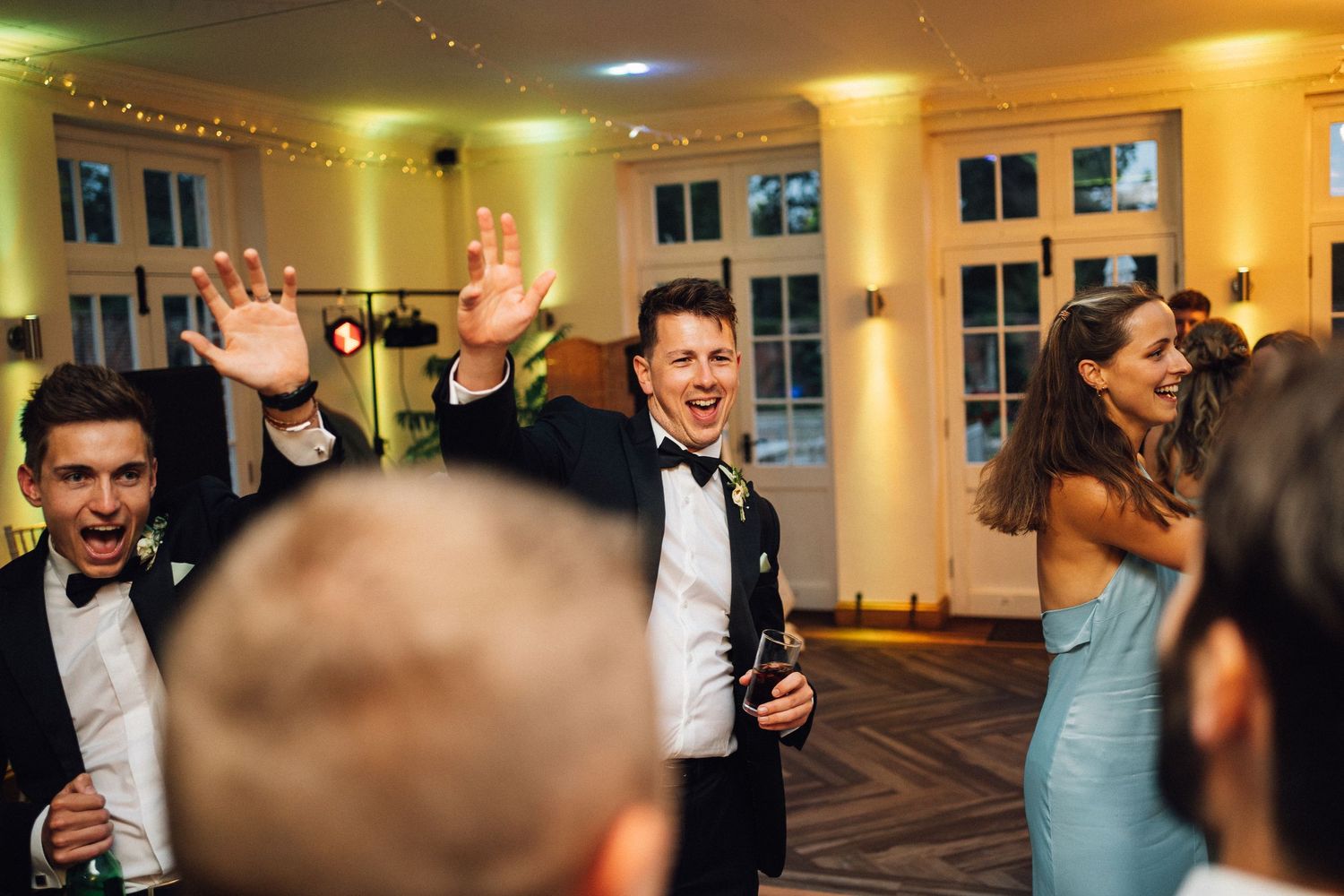 Wedding guests dancing and celebrating in brightly lit reception venue.