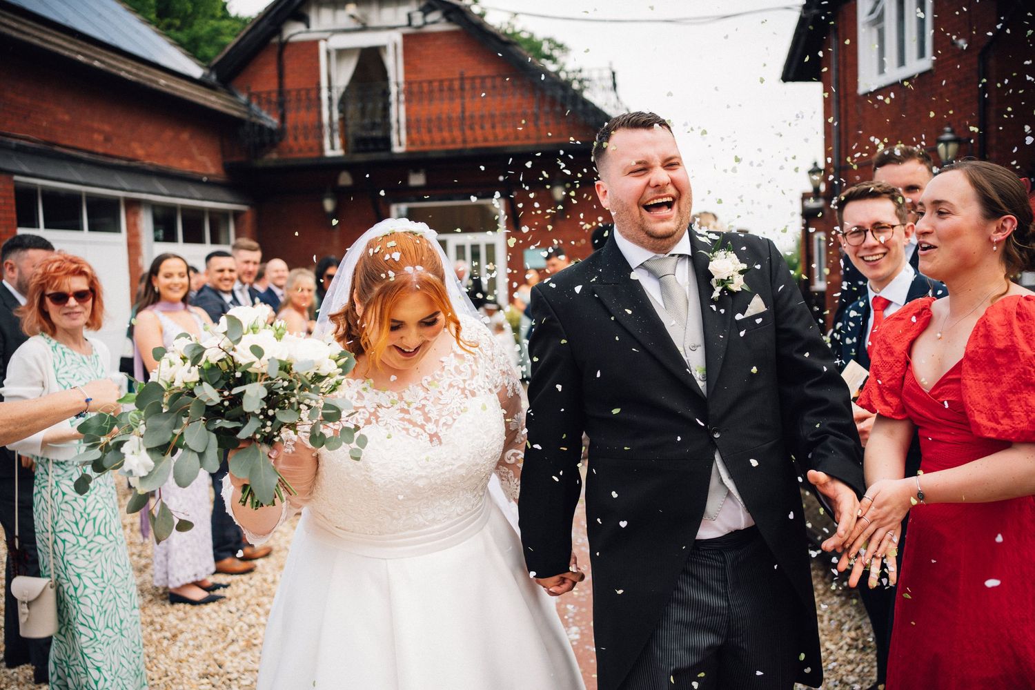 Joyful wedding celebration with guests throwing confetti outside a brick building.