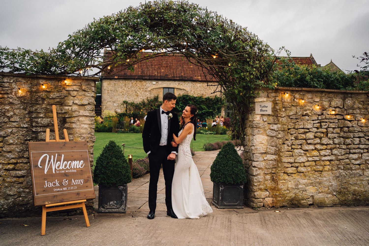 Outdoor wedding ceremony setup at a charming stone-walled venue with wooden welcome signs and natural landscaping.