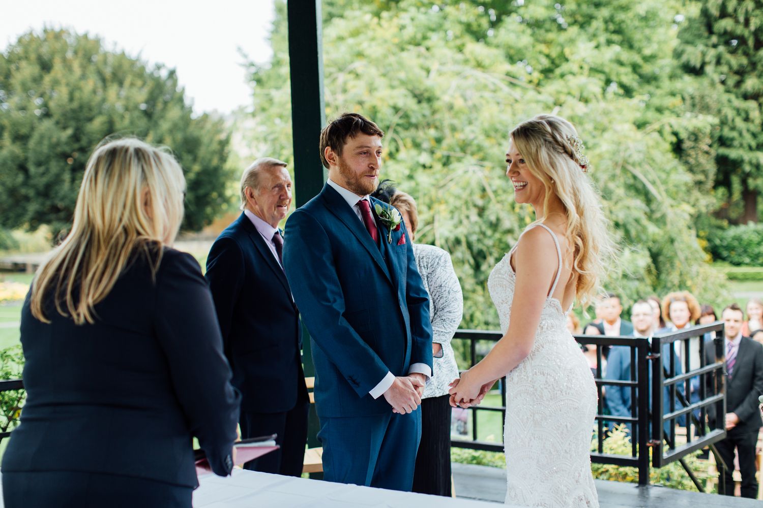 A wedding ceremony takes place outdoors with guests watching the couple exchange vows.