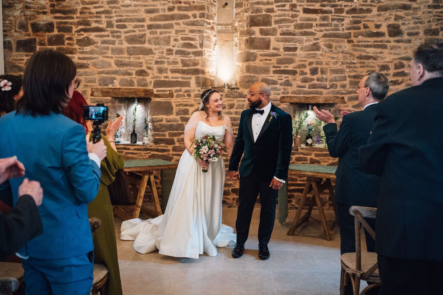 A wedding ceremony takes place in a rustic stone-walled venue with warm lighting and wooden decor.