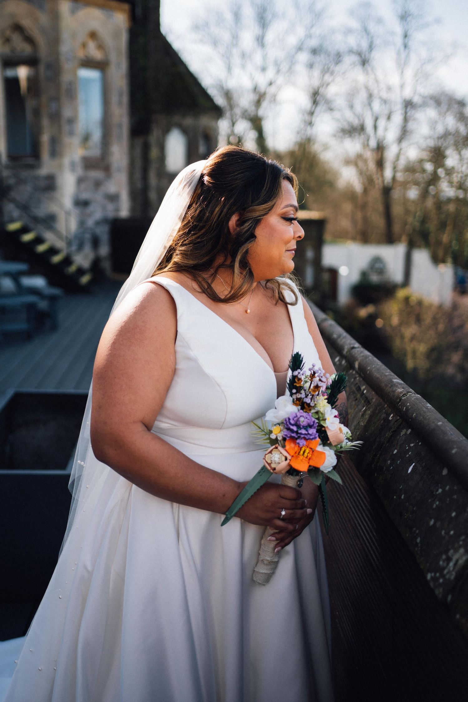 A bride in a white dress holds a colorful floral bouquet while standing outdoors on a sunny autumn day.