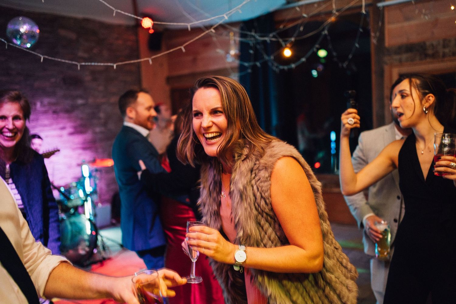 Wedding guests dancing and celebrating on dimly lit dance floor with colorful lighting effects.
