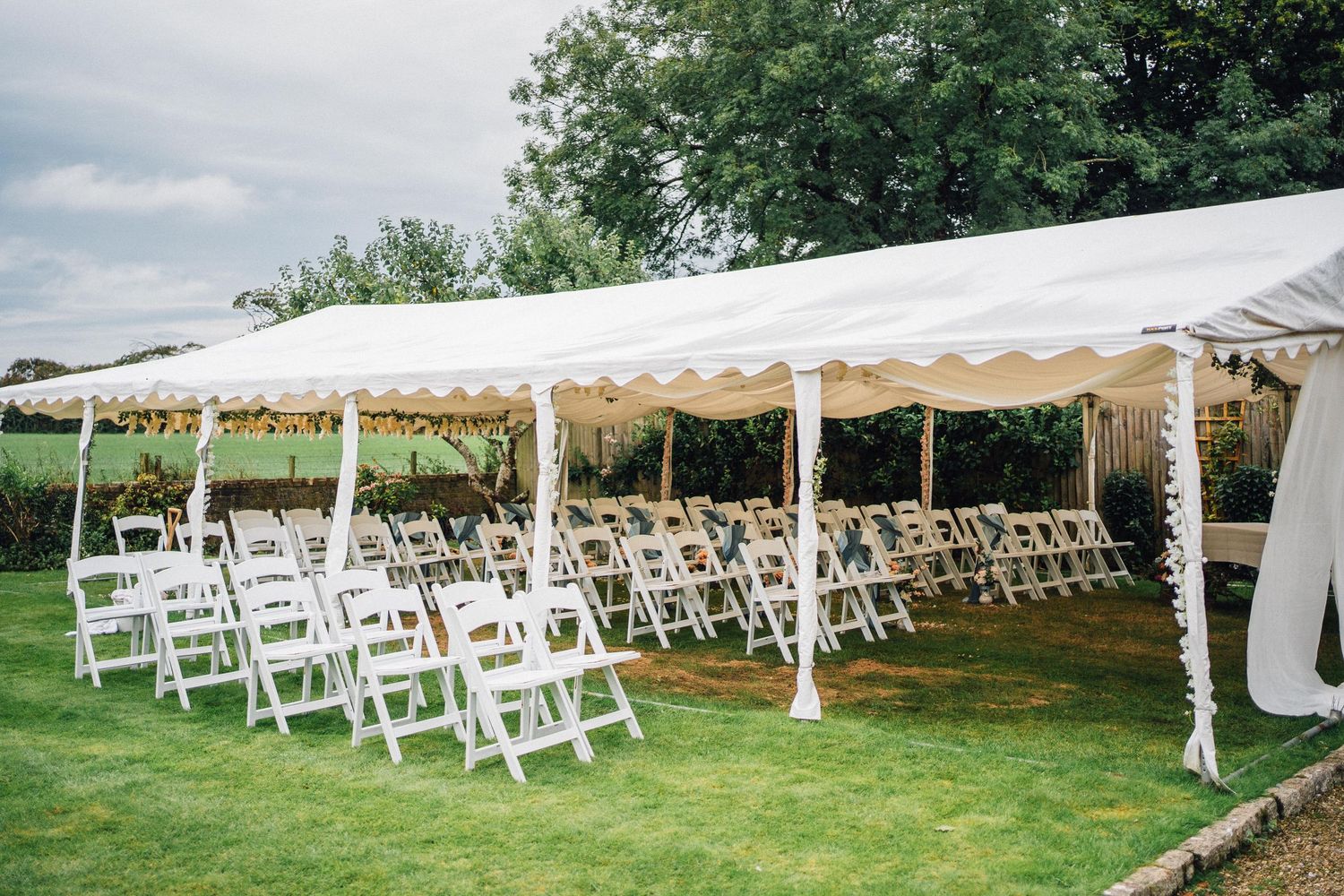 White wedding tent set up on a lawn with rows of folding chairs arranged for an outdoor ceremony.