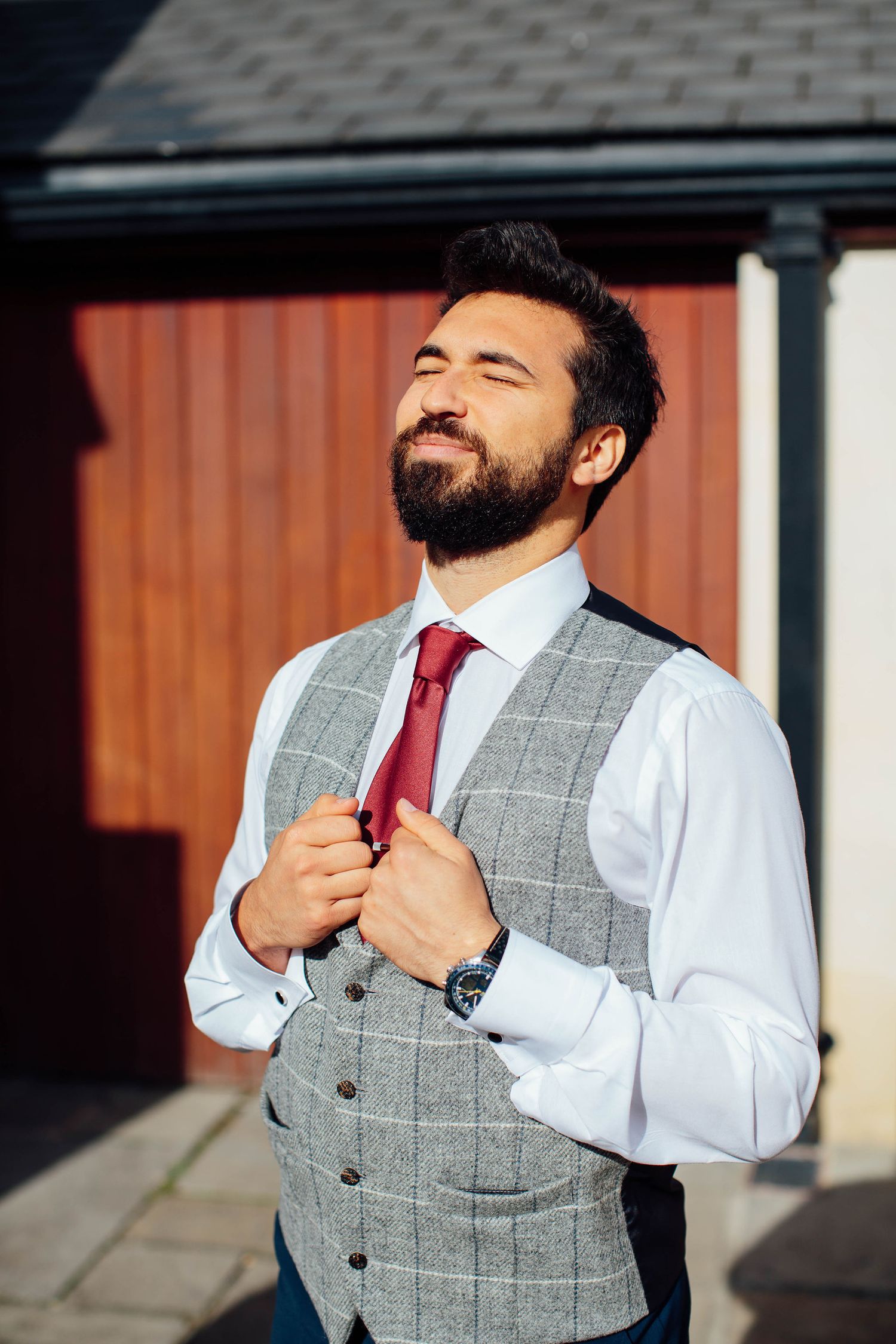 A series of photos showing someone adjusting a grey checkered vest and burgundy tie.