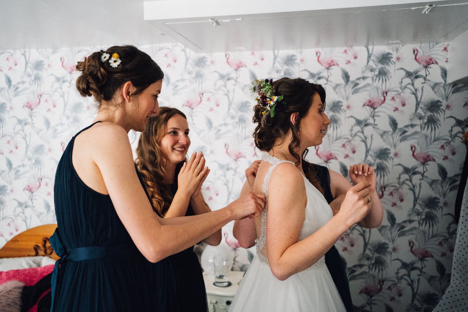 Wedding party members dancing and celebrating in a room with floral wallpaper.