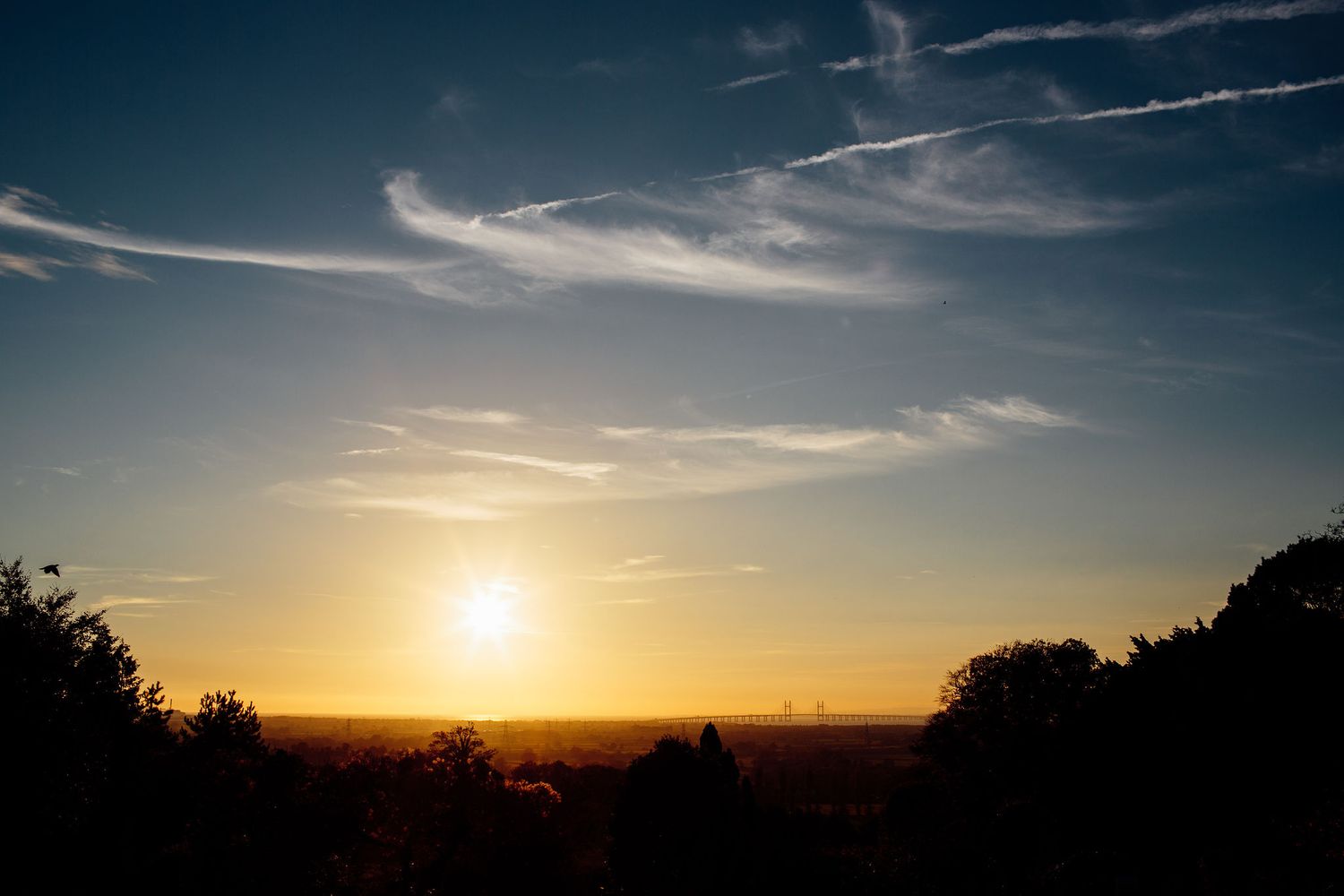 Dramatic sunset sky with streaking clouds and golden sunlight on the horizon.