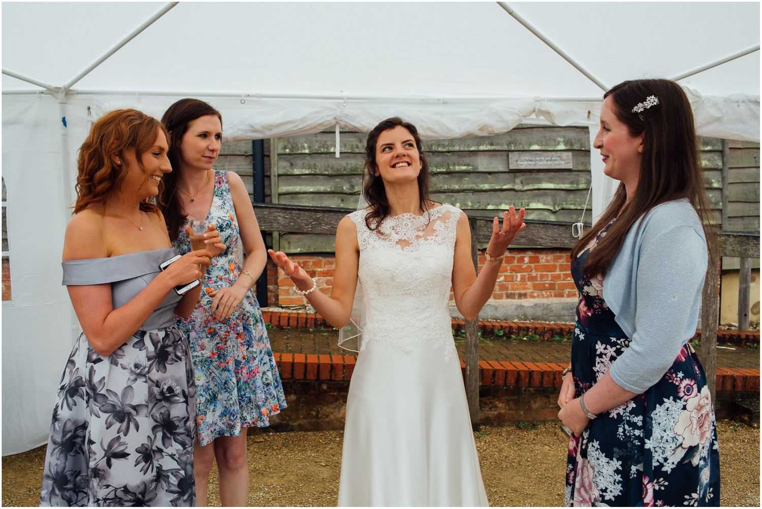 Wedding party in floral dresses enjoying drinks and conversation outdoors.