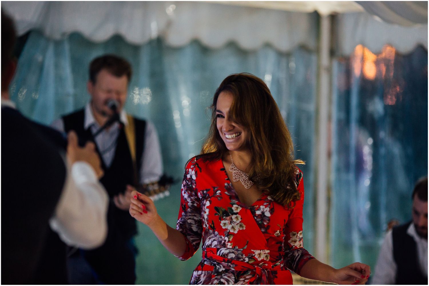 Wedding guests dancing and socializing at a tented evening celebration.