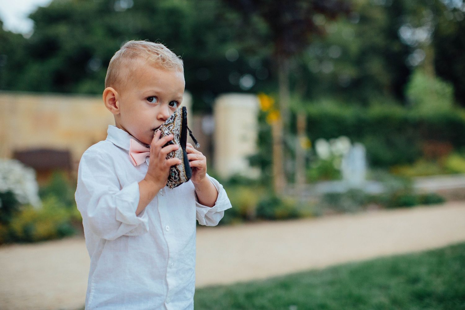 Young child in white shirt holding up a camera in a garden setting.