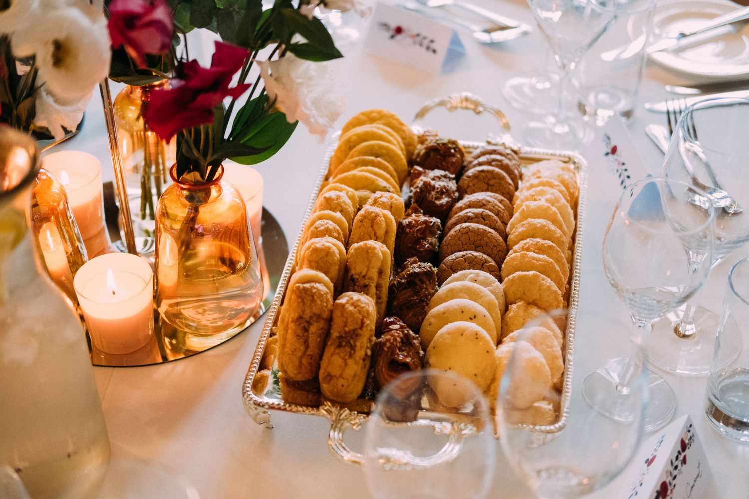 Close-up of wedding reception table settings with golden pastries and glowing candlelight.