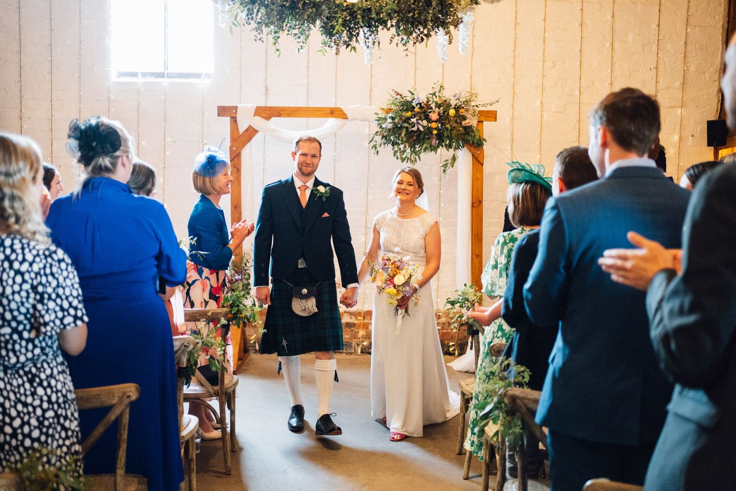 Wedding celebration in a converted barn with hanging greenery and ambient lighting.