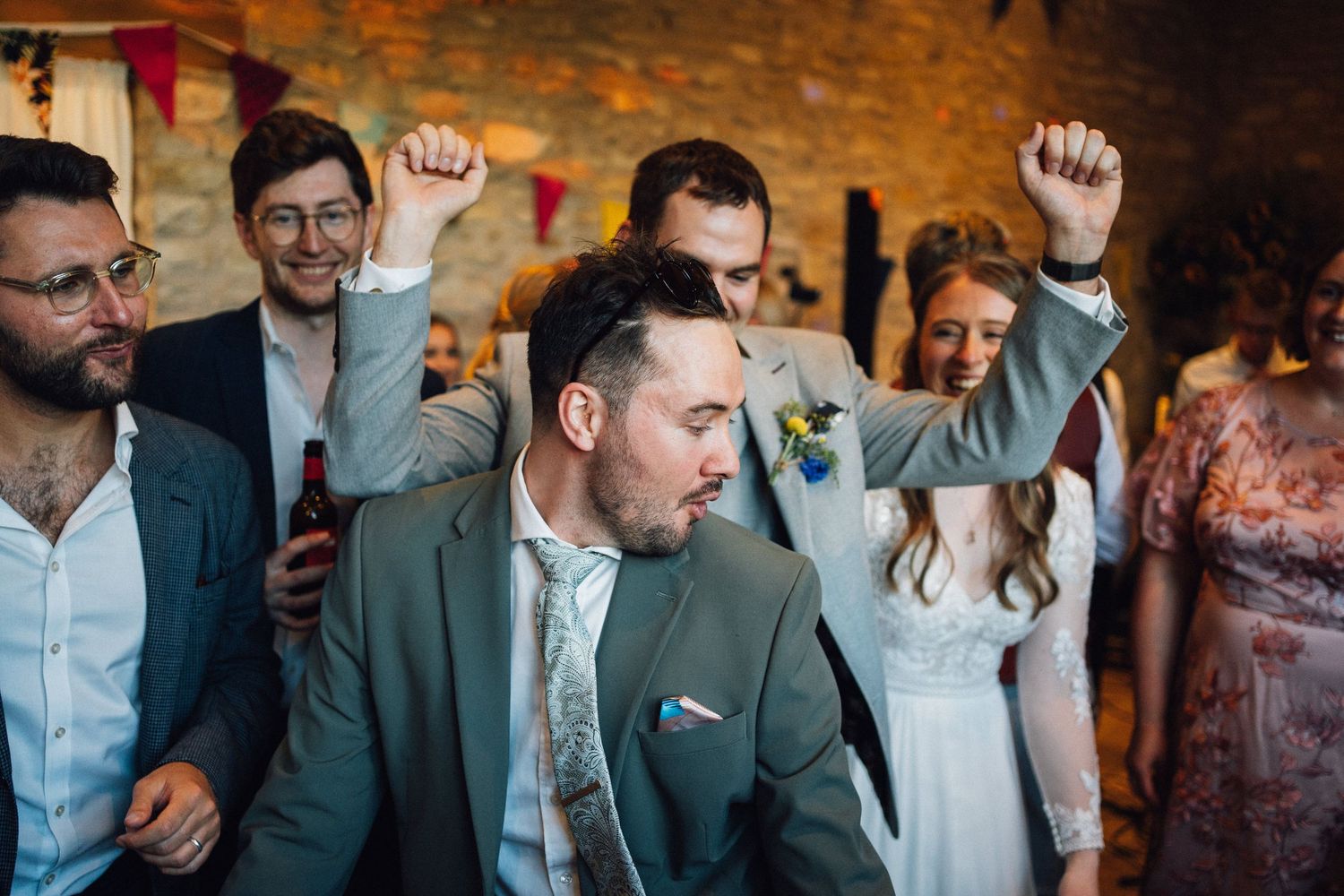 Wedding guests dancing and celebrating in a rustic stone barn with ambient lighting.