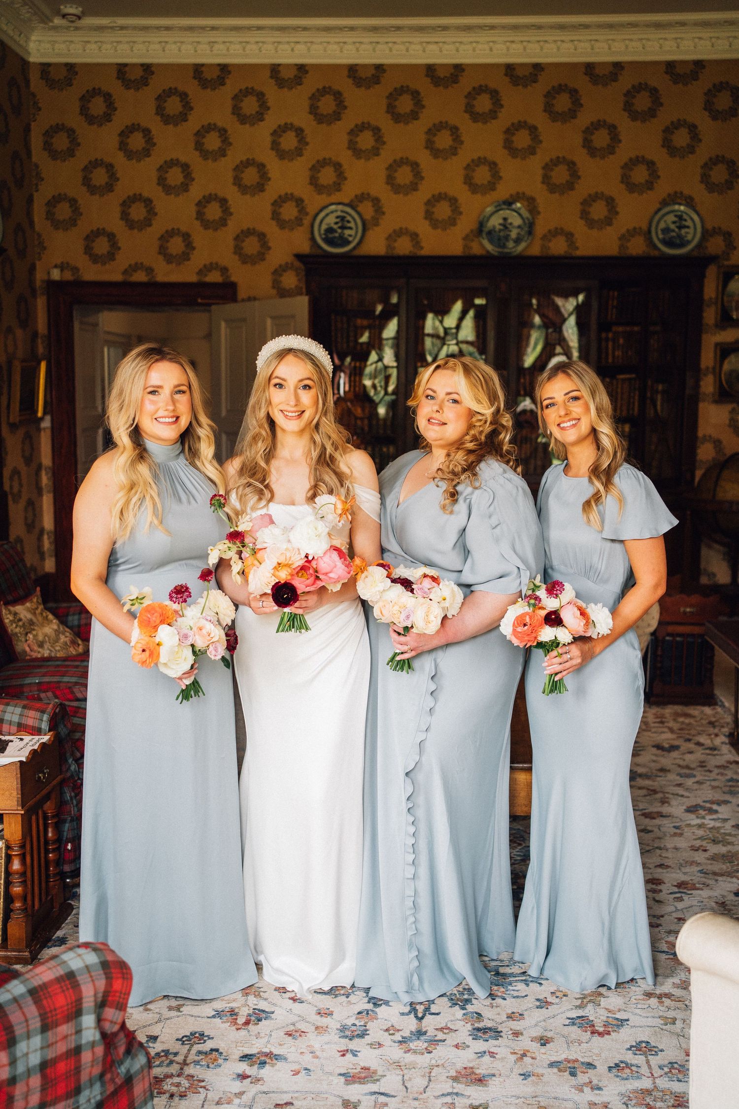 Bridal party in pale blue dresses poses with bouquets against patterned wallpaper.