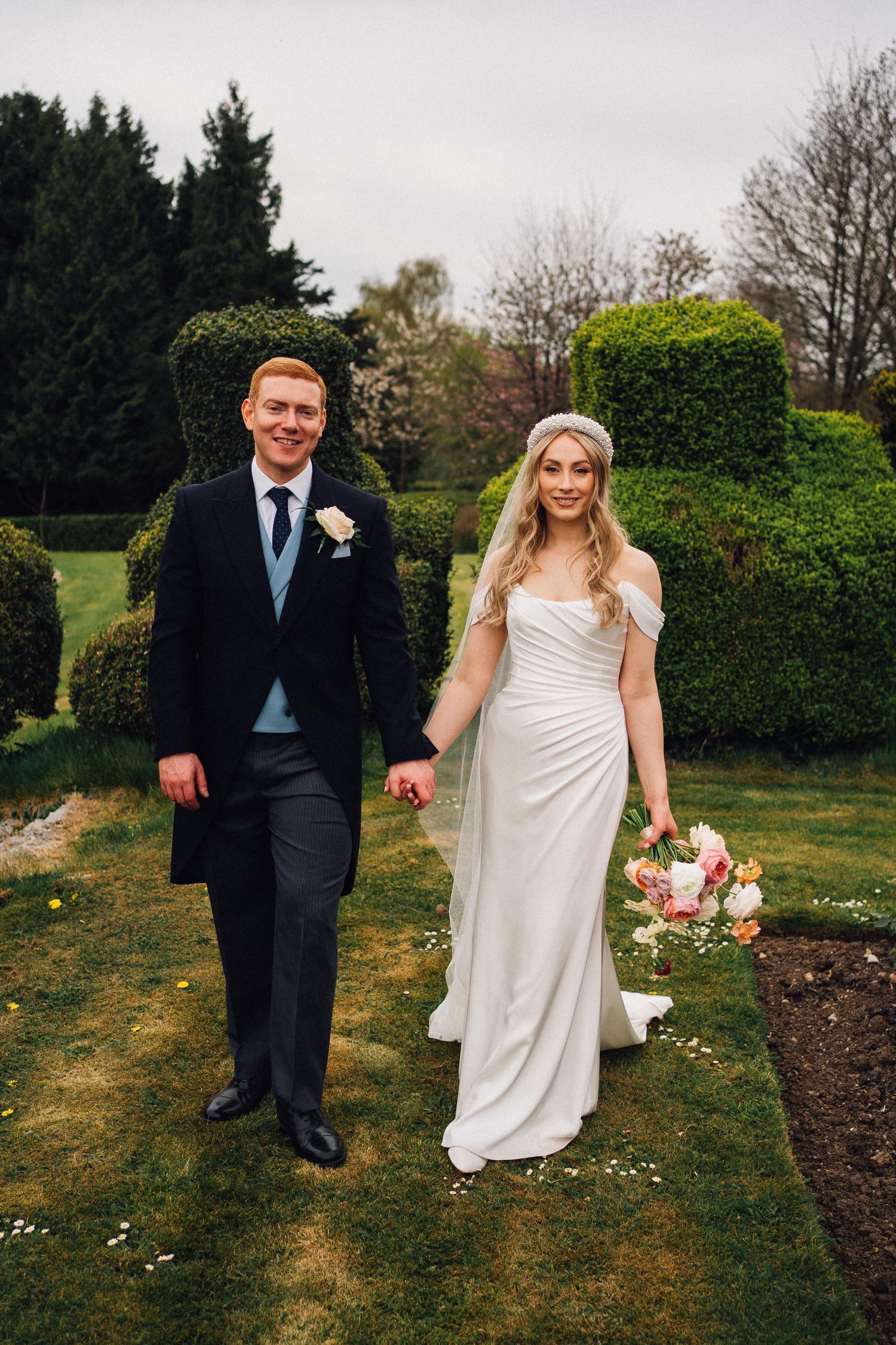 A wedding couple walks hand in hand through a manicured garden on their special day.