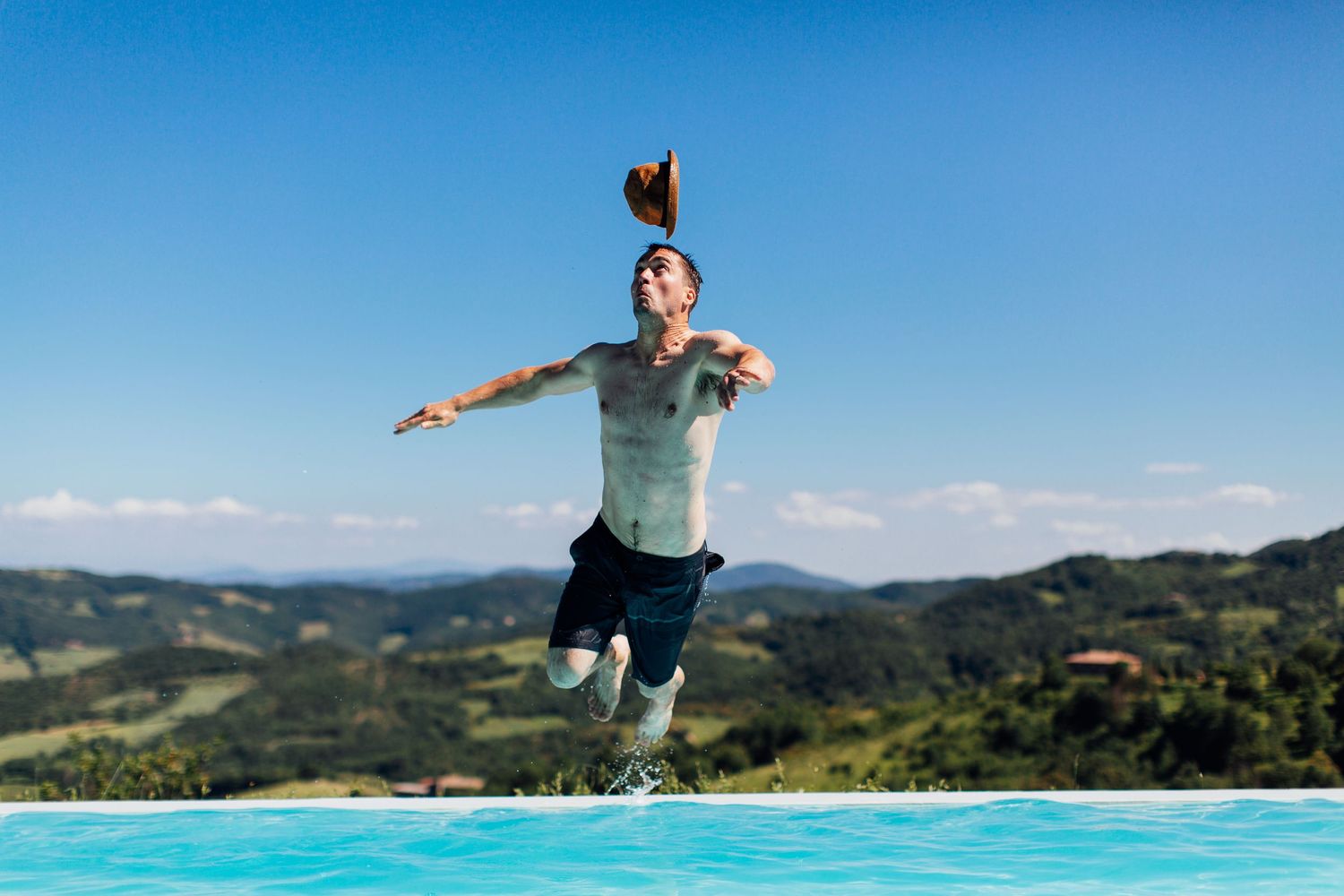 Person jumping playfully above an infinity pool with mountains in the background.