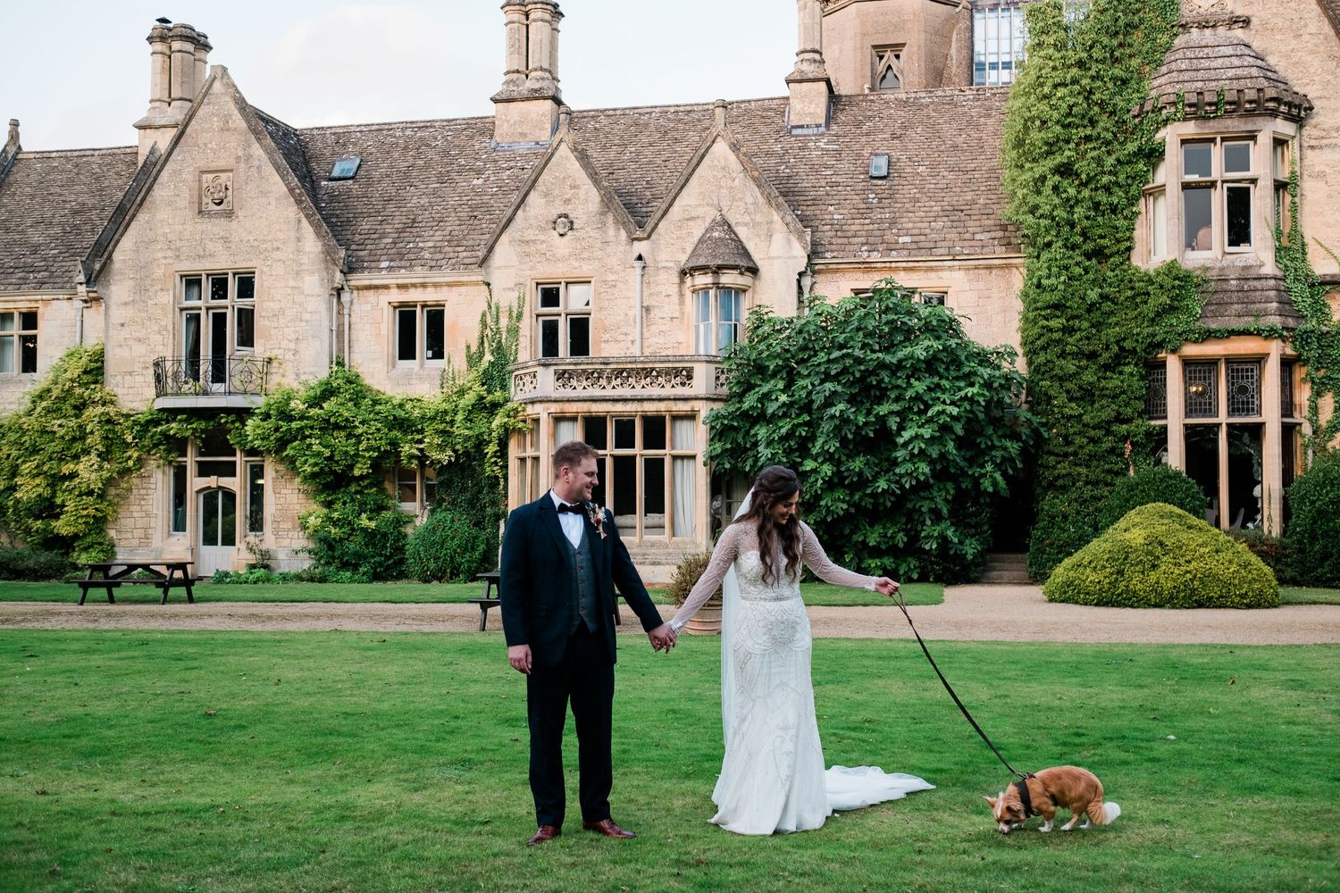 Wedding couple poses on the lawn of an elegant stone manor house with beautiful landscaping.