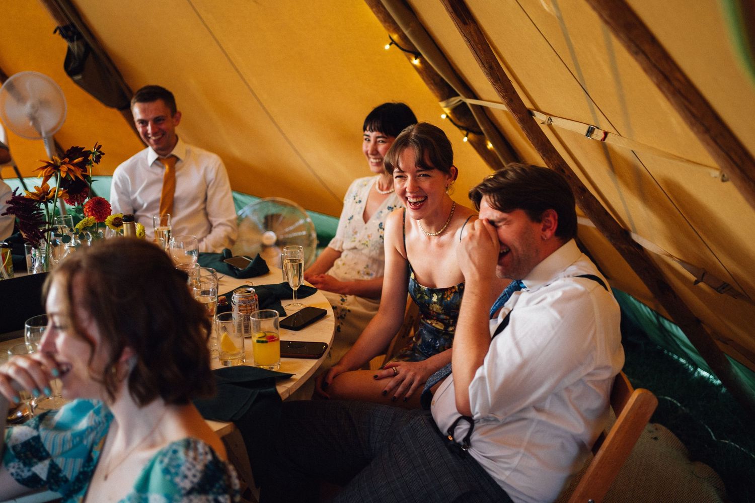 Wedding guests enjoy dancing and celebrating under a warm-lit tent during an evening reception.