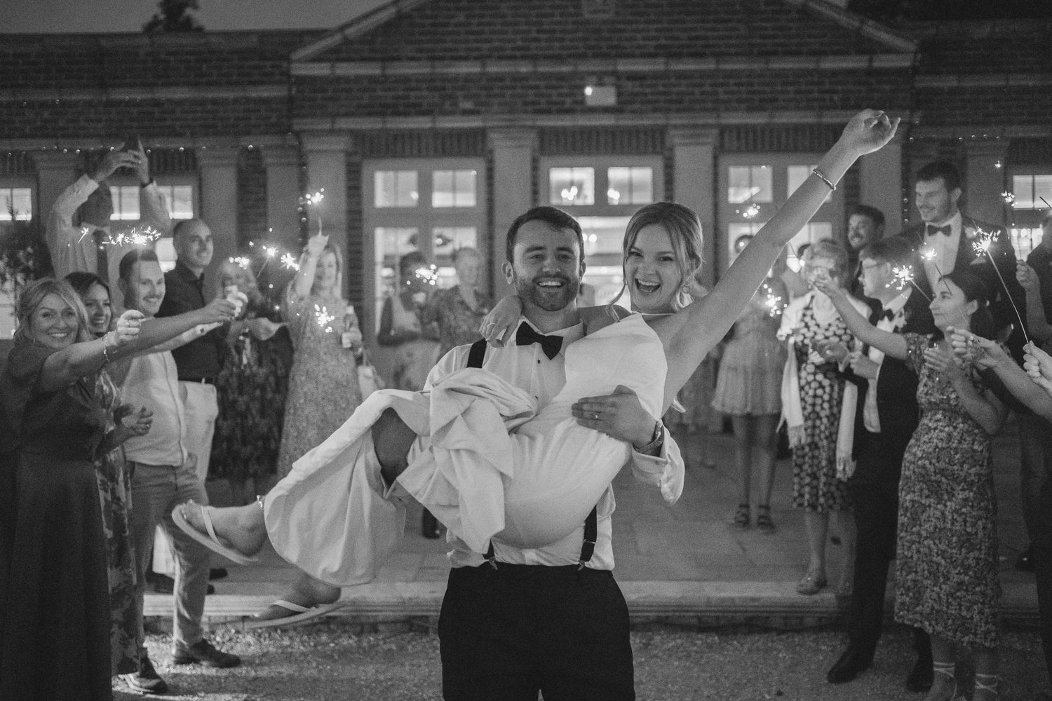 Black and white photo of wedding guests dancing and celebrating at indoor reception.