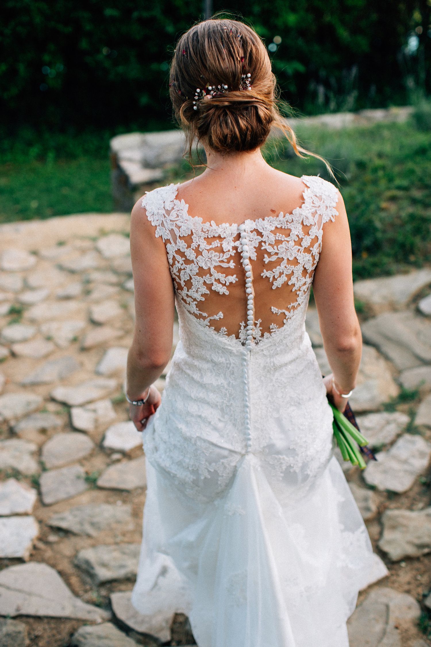 Delicate lace details on the back of a white wedding dress with sheer illusion neckline and button closures.