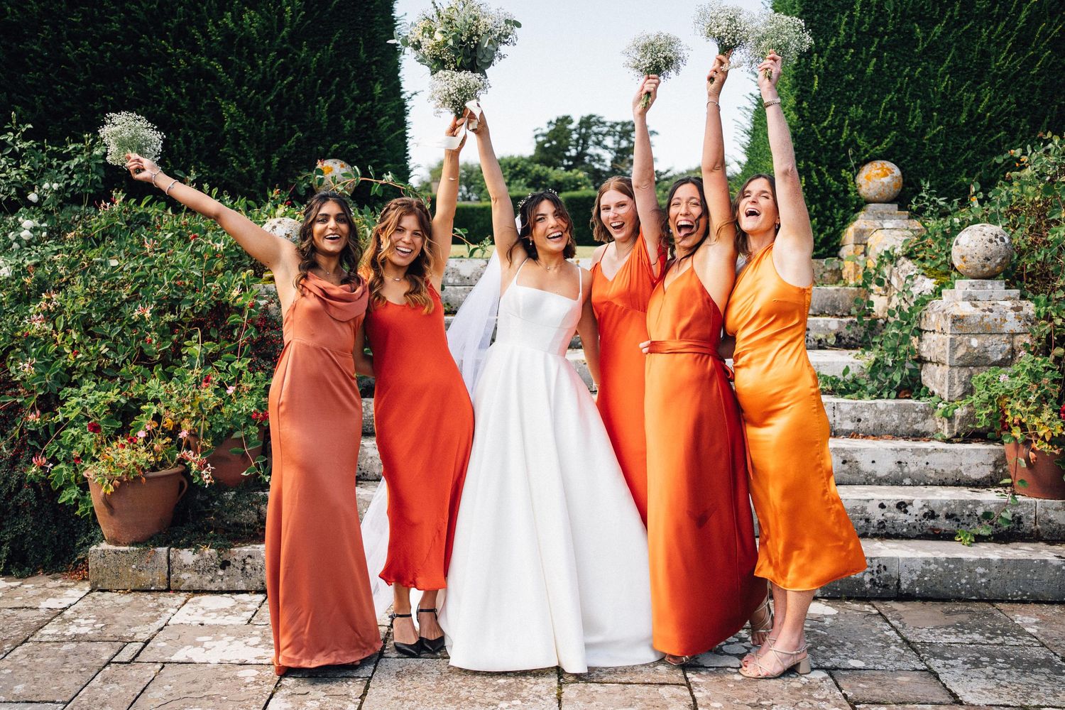 A wedding party in orange and white dresses poses together in an outdoor garden setting at an Estate in Bristol
