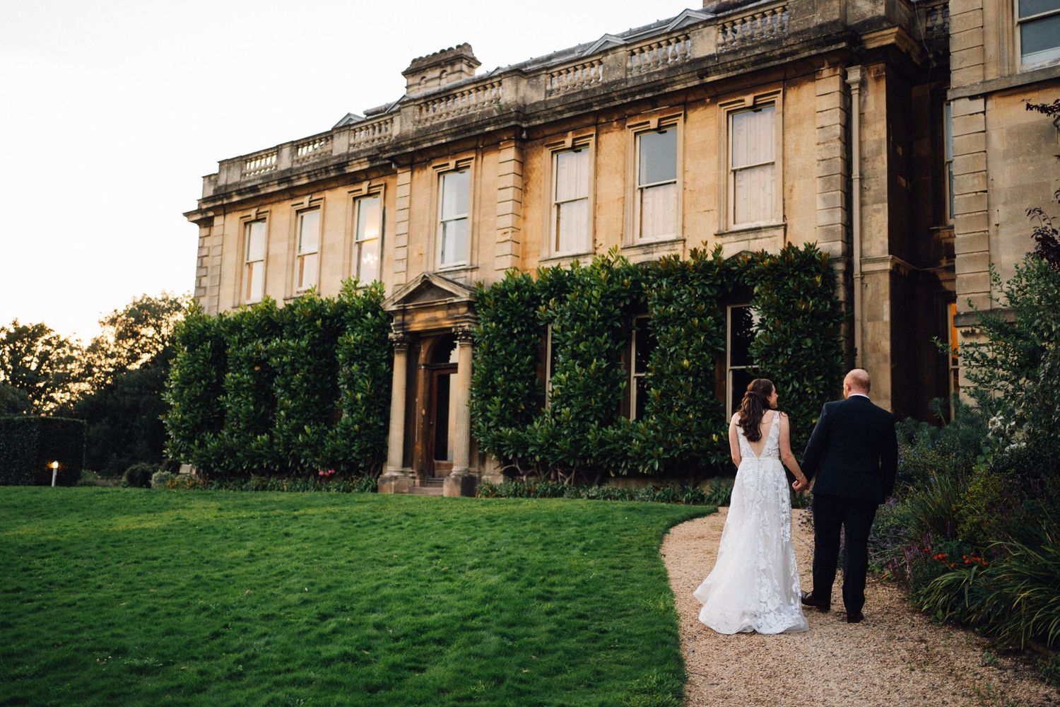 Elegant wedding couple walks along a grand stone colonnade at sunset during their outdoor celebration.