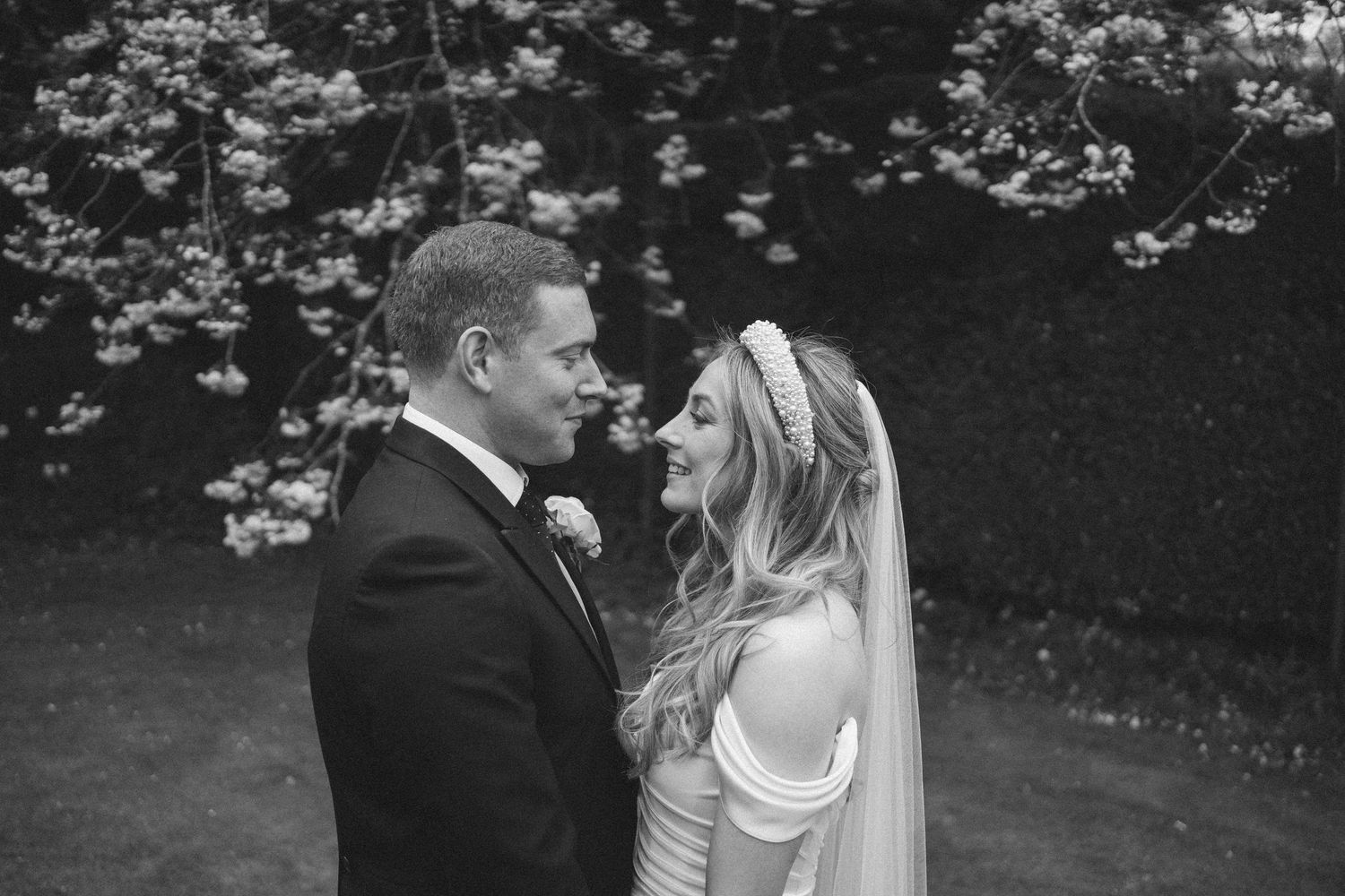 Bride and groom share intimate moments during their wedding photoshoot under blooming cherry blossoms.