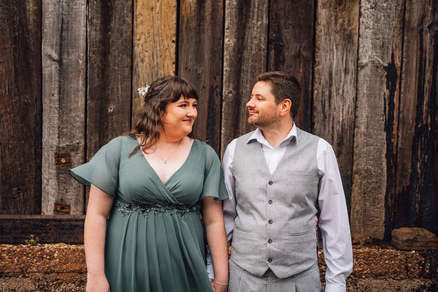 A couple shares a happy moment together while standing in front of a rustic wooden wall.